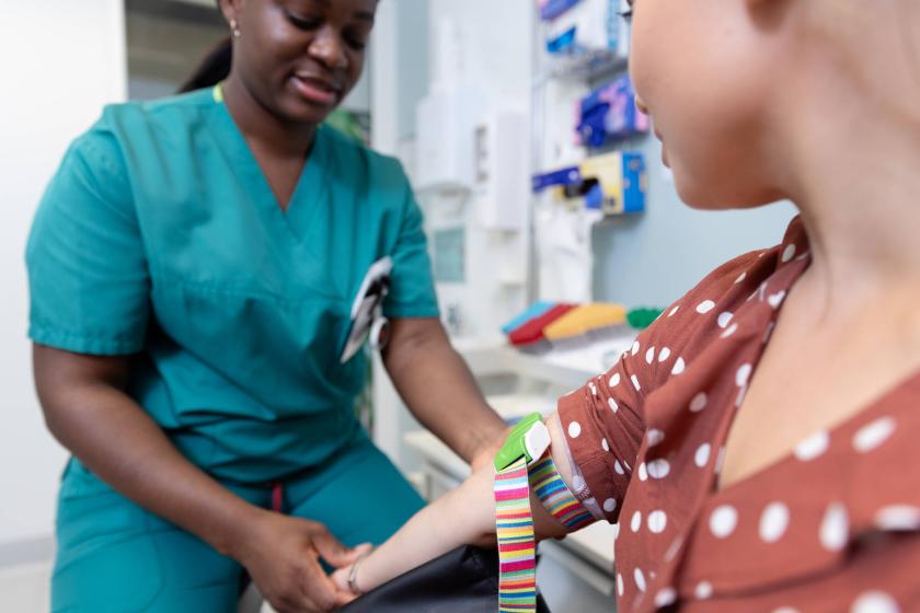 A laboratory nurse taking a sample from a patient. Only the patient’s arm and part of the face are visible. 