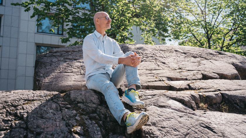 HUSin potilastarinan haastateltava Sakari istumassa kalliolla kesäpäivänä. 