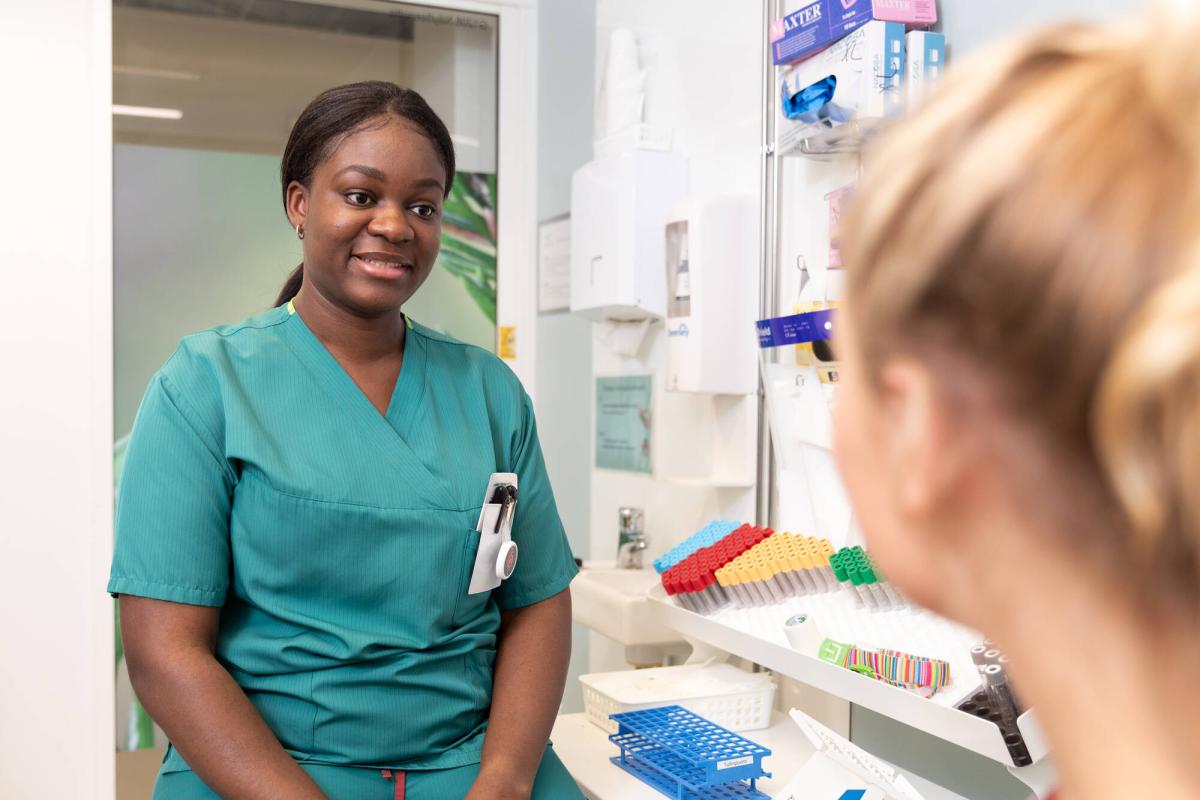 En laboratorieskötare diskuterar med patienten. Patienten syns delvis bakifrån.